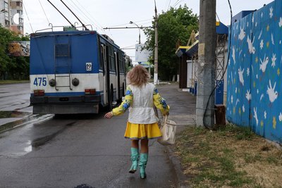 Жінка у вишиванці біжить до тролейбуса поряд з бетонним укриттям на зупинці, розмальованим у стилі робіт художниці Поліни Райко