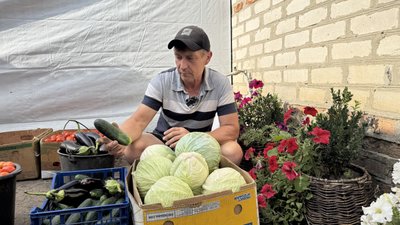 Фермер показує врожай огірків, капусти, баклажанів