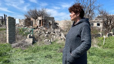 Місцева жителька Олена поруч із пошкодженим будинком Місцева жителька Олена поруч із пошкодженим будинком