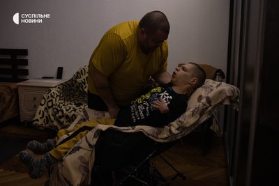 Тарас перекладає сина Богдана з важкою формою ДЦП з ліжка в крісло колісне. Життя Богдана залежить від людей, які його оточують Тарас перекладає сина Богдана з важкою формою ДЦП з ліжка в крісло колісне. Життя Богдана залежить від людей, які його оточують