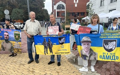 Учасники акції тримають плакати з закликами та прапори з фотографіями рідних Учасники акції тримають плакати з закликами та прапори з фотографіями рідних