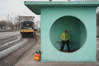 Жінка чекає транспорт на зупинці на київській трасі на Харківщині, поки поруч ремонтують дорогу Жінка чекає транспорт на зупинці на київській трасі на Харківщині, поки поруч ремонтують дорогу