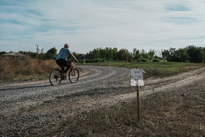 Чоловік їде велосипедом по розмінованій дорозі Чоловік їде велосипедом по розмінованій дорозі