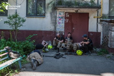 Втомлені рятувальники та поліцейські відпочивають у тіні поміж роботами з пошуку людей під завалами у Кременчуці, червень 2022 року. Російські війська 27 червня вдарили ракетою по торговельно-розважальному центру "Амстор" у Кременчуці на Полтавщині.