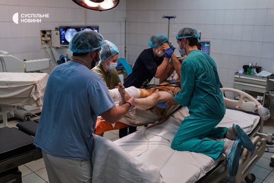 Хірурги разом із медсестрами перекладають військового з операційного столу на ліжко, Київ, січень 2023 року. Операція тривала кілька годин. Боєць був поранений на Донбасі під час обстрілу, розповідають лікарі.