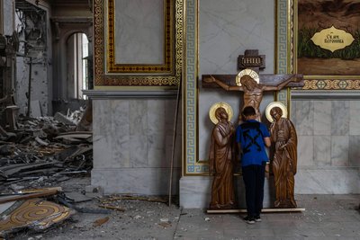 Хлопчик цілує статую Ісуса під час прибирання у зруйнованому російською ракетою соборі в Одесі