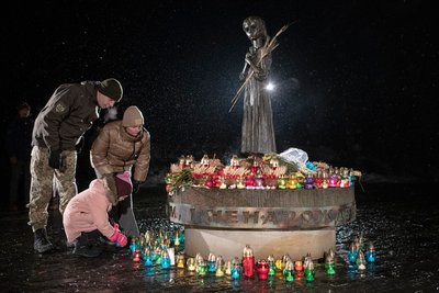 Військовий з сім'єю запалює свічки біля пам’ятника жертвам Голодомору у Києві, 26 листопада 2022
