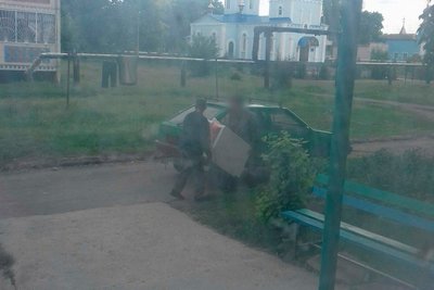 Підозрювані окупанти виносять пральну машину в автомобіль у Пролісному