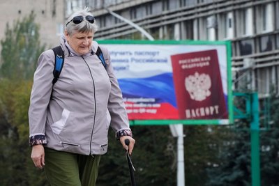Жінка проходить повз білборд із закликом отримувати російський паспорт у Луганську Жінка проходить повз білборд із закликом отримувати російський паспорт у Луганську