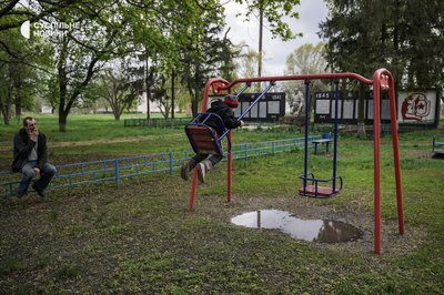 Олексій зі своїм сином на гойдалках в центрі села Підвисоке, Харківщина, квітень 2023 року.
