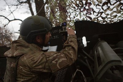Військовий наводить гармату артилерійською бусоллю