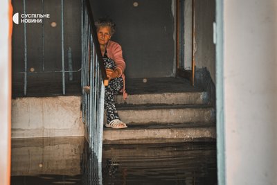 Жінка сидить у підтопленому підʼїзді у Херсоні