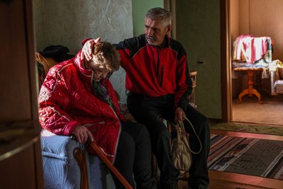 Олексій Русак допомагає своїй дружині Галині одягатися під час евакуації з Куп'янську на Харківщині, 8 березня 2023 року