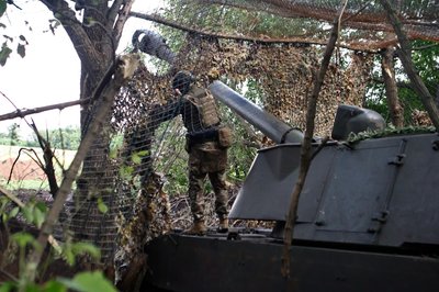 Військовий прикриває маскувальною сіткою САУ на вогневій позиції Військовий прикриває маскувальною сіткою САУ на вогневій позиції