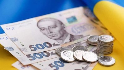 Паперові та металеві гроші на фоні прапора України