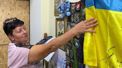 Наталія дивиться на розписаний військовими та волонтерами прапор. На початку великої війни староста сіл Лимани та Лупареве продовжувала піклуватися про громаду. Попри щоденні обстріли, вона забезпечила підвіз медикаментів та організувала трансфер до міста Наталія дивиться на розписаний військовими та волонтерами прапор. На початку великої війни староста сіл Лимани та Лупареве продовжувала піклуватися про громаду. Попри щоденні обстріли, вона забезпечила підвіз медикаментів та організувала трансфер до міста