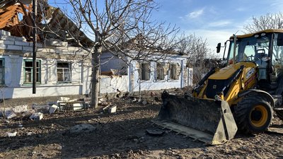 Трактор працює на вулиці, де внаслідок обстрілів пошкоджені будинки