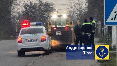 Двоє людей у формі та одна людина у цивільному одязі стоять на тротуарі біля автівок