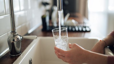 Крупний план руки, яка наливає чисту воду з-під крана у склянку. Фото ілюстративне