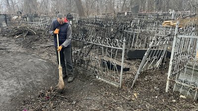 Працівник кладовища прибирає біля зруйнованих могил