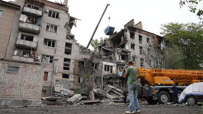 Чоловік стоїть перед пошкодженою багатоповерхівкою