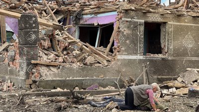 Жінка схилилася над тілом загиблого біля зруйнованого будинку внаслідок російського