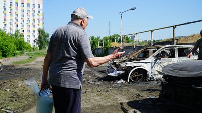 Чоловік дивиться на потрощені автівки у Шевченківському районі Харкова після влучання