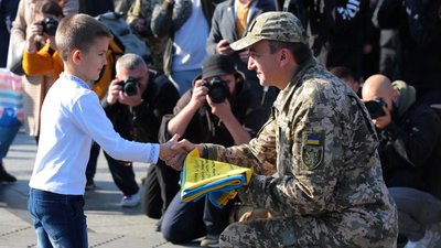 Хлопчик дарує військовому прапор України із побажаннями Хлопчик дарує військовому прапор України із побажаннями