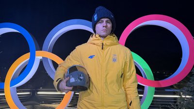 Владислав Гераскевич тримає шолом на фоні олімпійський кілець у Кортіні-д'Ампеццо