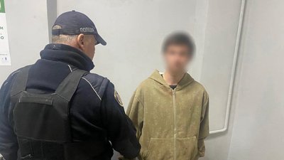 Поліцейський у тактичному жилеті супроводжує затриманого 19-річного чоловіка