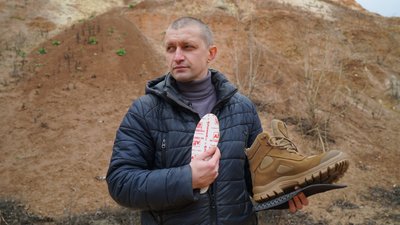 Харківський волонтер тримає в руках військове взуття і бронеустілки
