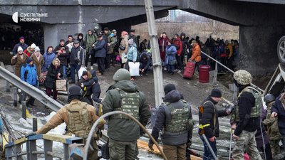 Бійці Територіальної оборони, поліцейські та волонтери допомагають цивільним перейти через підірваний Романівський міст через річку Ірпінь, березень 2022 року.