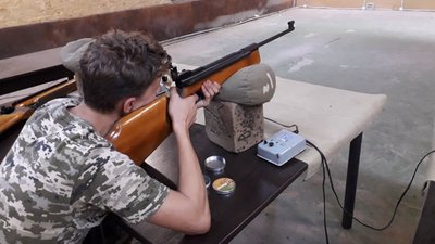 Стріляють по мішенях сидячи за столом з опорою ліктями на стіл зі спортивної пневматичної гвинтівки Стріляють по мішенях сидячи за столом з опорою ліктями на стіл зі спортивної пневматичної гвинтівки