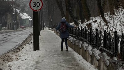 Дитина тримається за поручень огорожі, щоб не послизнутися на тротуарі