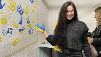 Жінка біля стіни з жовто-синіми долонями