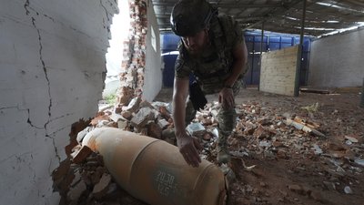 Поліцейський оглядає бомбу, що не розірвалася після авіаудару по складу в Білому Колодязі
