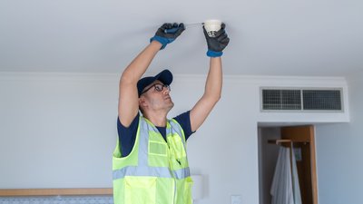 Фахівець встановлює датчик диму на стелі