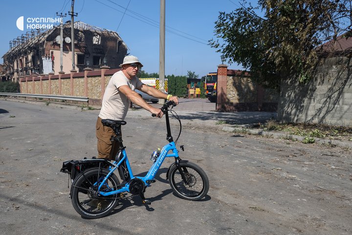 Чоловік спостерігає за роботою саперів неподалік частково згорілої будівлі місцевого ресторанного комплексу у селі Мила на Київщині, де сталась пожежа на військових складах після російської атаки реактивними «шахедами», 29 серпня 2026 року